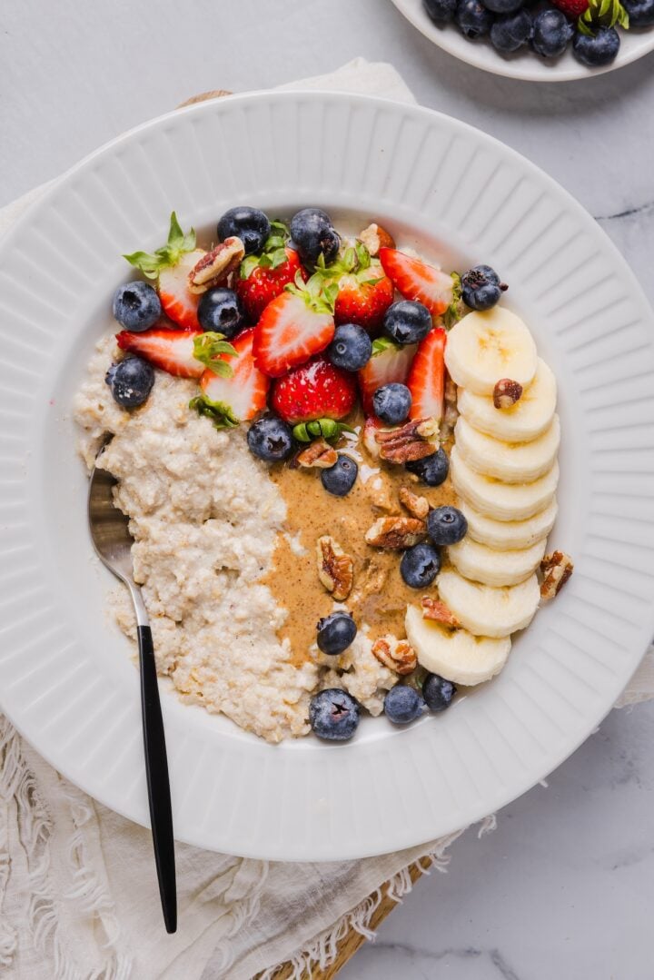 Creamy, high-protein oatmeal that actually tastes good! This easy recipe delivers 32 grams of protein per bowl & comes out perfect every time. Protein oatmeal in a small white bowl, topped with berried, banana, and nut butter.