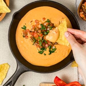 Viral high-protein cottage cheese queso dip with a woman's hands dipping into the dip with a tortilla chip.