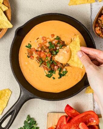 Viral high-protein cottage cheese queso dip with a woman's hands dipping into the dip with a tortilla chip.