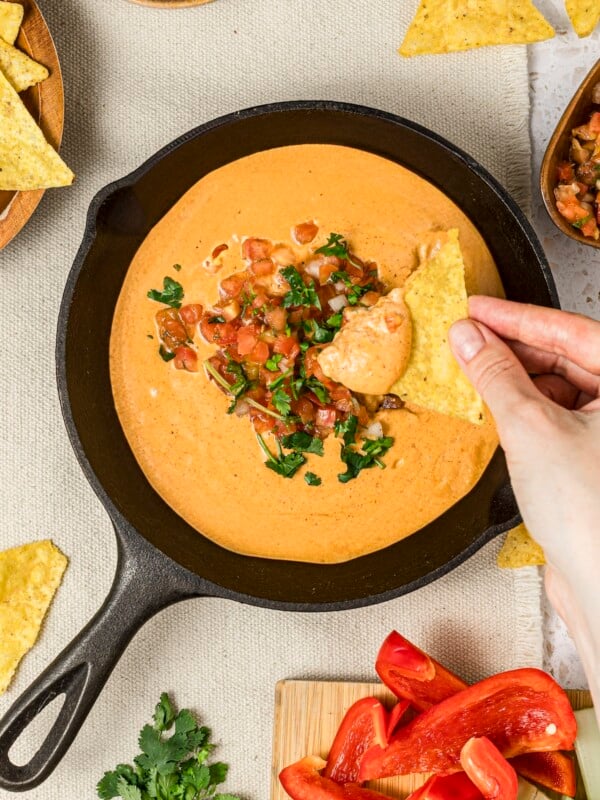 Viral high-protein cottage cheese queso dip with a woman's hands dipping into the dip with a tortilla chip.