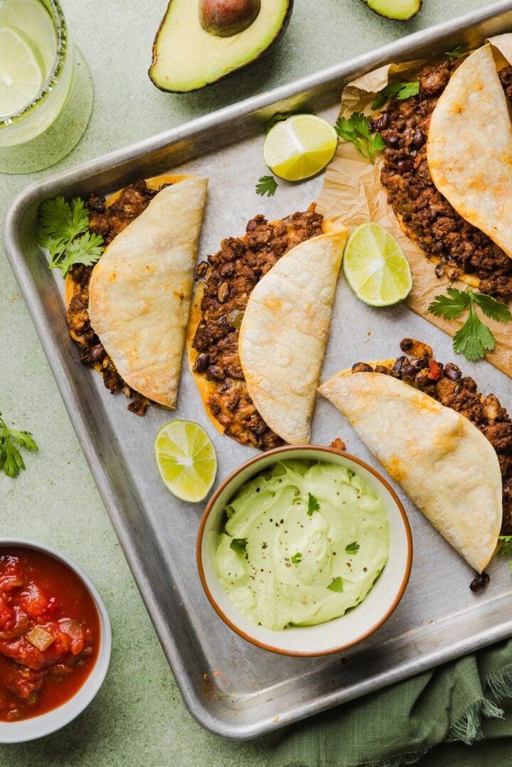Crispy beef tacos with avocado lime crema on a sheet pan.
