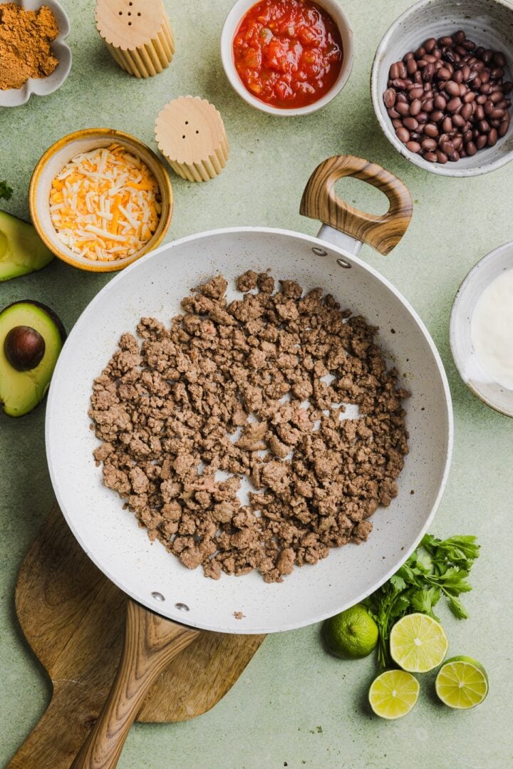 Ground beef cooked and crumbled in a white pan.