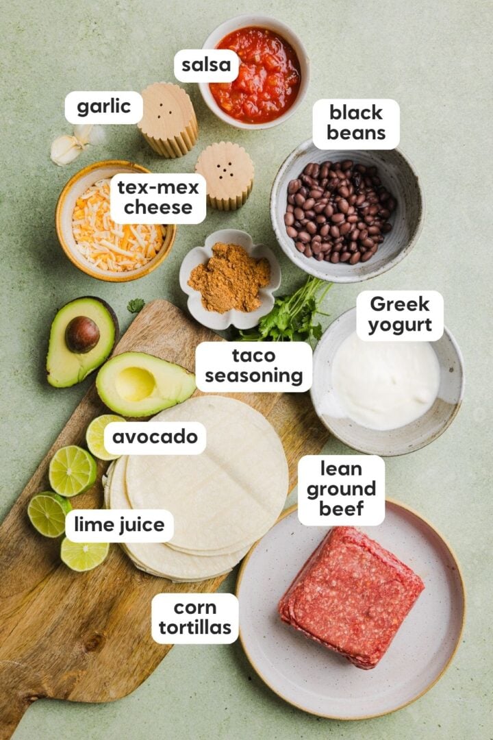 Ingredients for crispy beef tacos displayed in small bowls on a green kitchen counter.