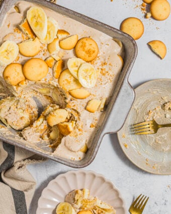 Dairy-free banana pudding in a baking dish, being scooped onto a serving plate.