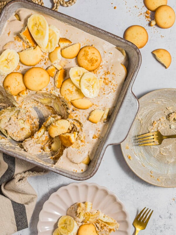 Dairy-free banana pudding in a baking dish, being scooped onto a serving plate.