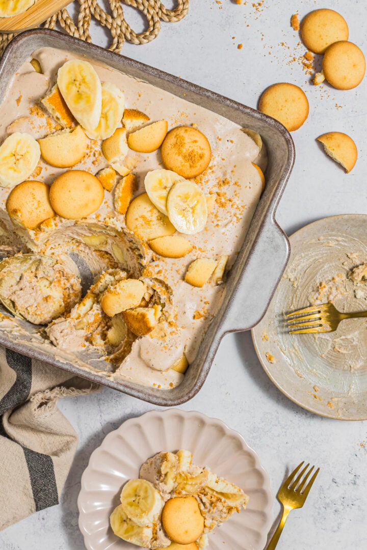Dairy-free banana pudding in a baking dish, being scooped onto a serving plate.