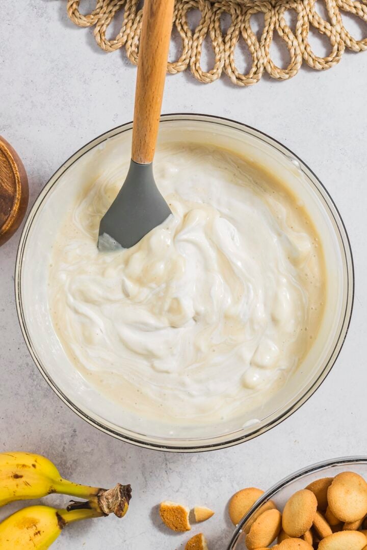 Whipped cream mixed with banana pudding in a large glass mixing bowl.