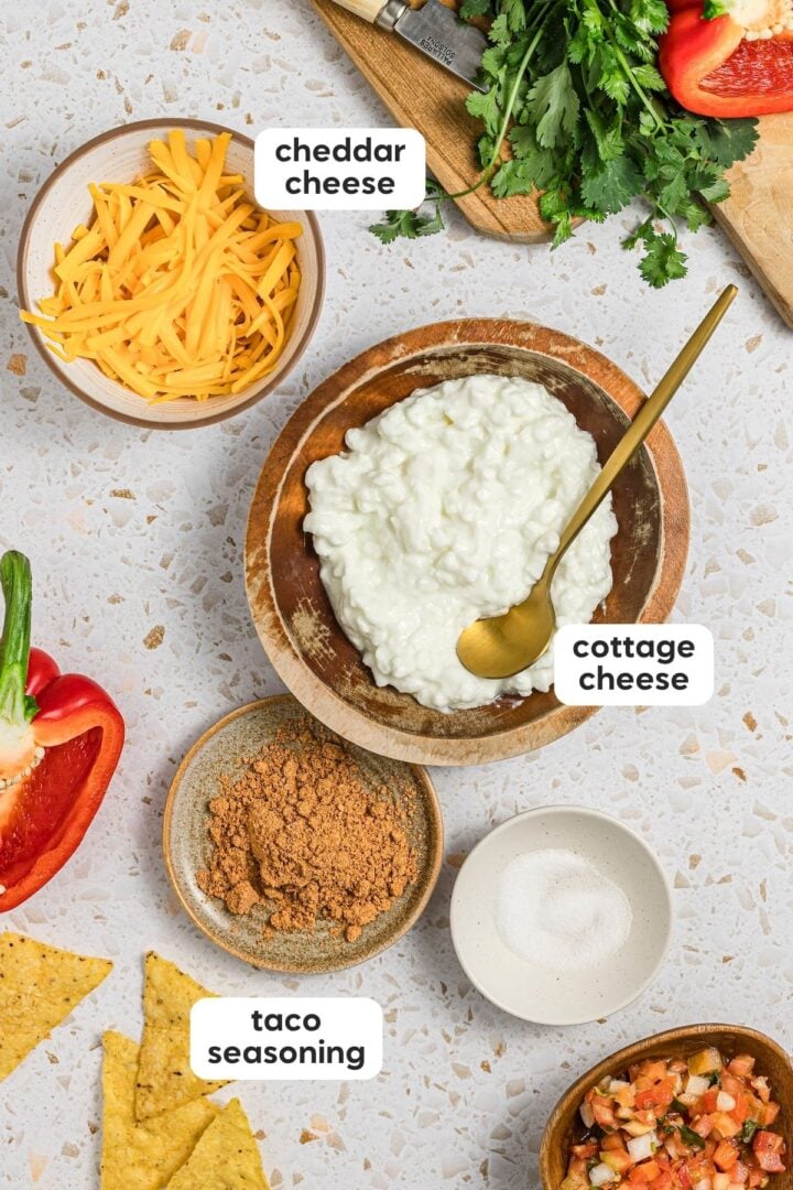 Labeled photo of the ingredients in high-protein cottage cheese queso dip, displayed in small bowls on a kitchen counter.