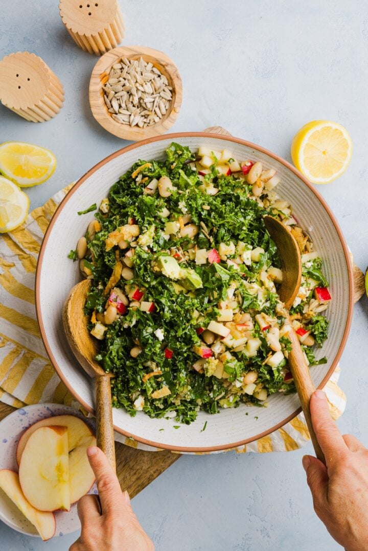 Kale white bean salad being tossed with wooden salad tongs in a large mixing bowl.