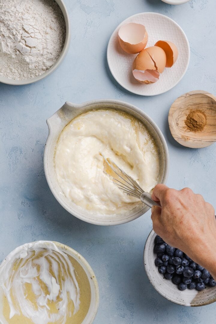 Wet ingredients for whole wheat blueberry muffins being whisked by a woman's hands in a large white bowl.