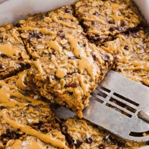 Peanut butter baked oats sliced into squares in a baking pan, and drizzled with extra peanut butter.