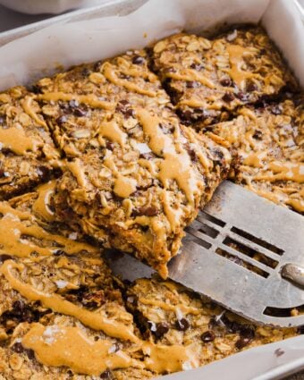 Peanut butter baked oats sliced into squares in a baking pan, and drizzled with extra peanut butter.