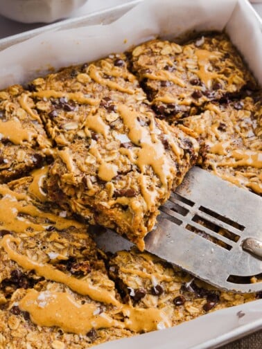 Peanut butter baked oats sliced into squares in a baking pan, and drizzled with extra peanut butter.