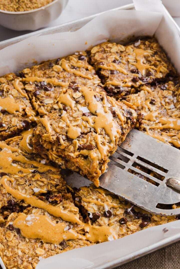 Peanut butter baked oats sliced into squares in a baking pan, and drizzled with extra peanut butter.
