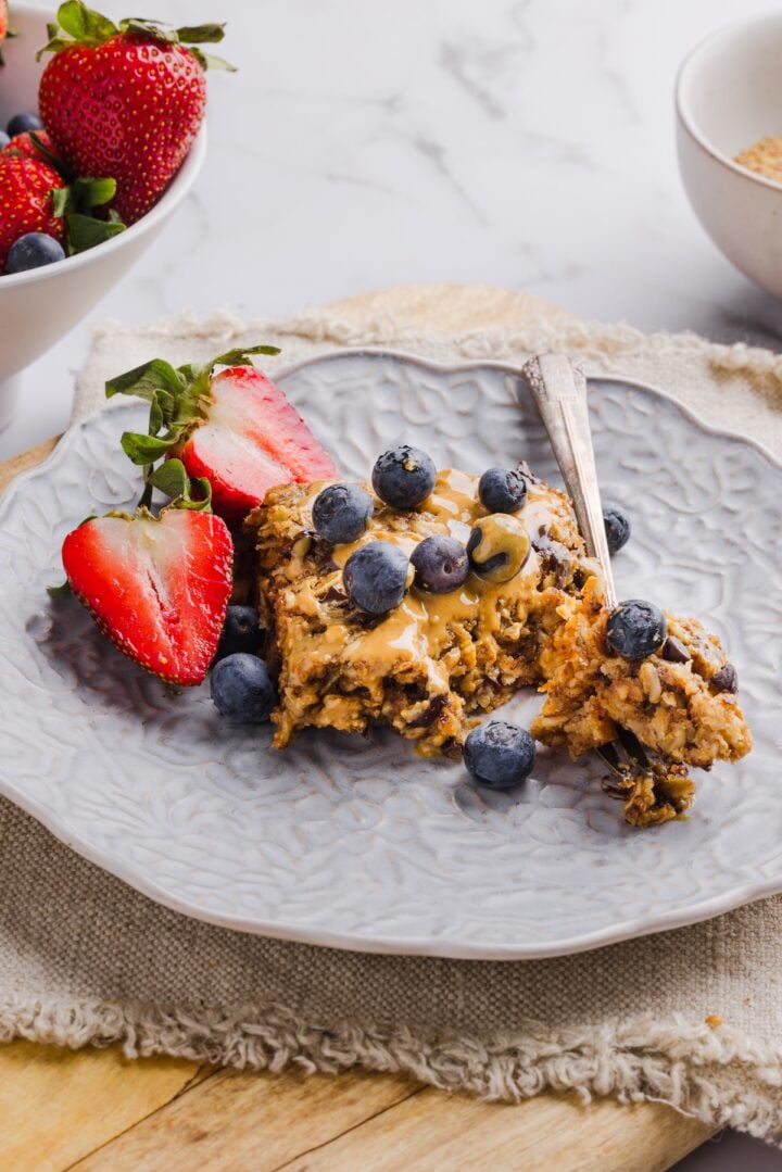 A square of peanut butter baked oats on a grey plate with peanut butter and berries.