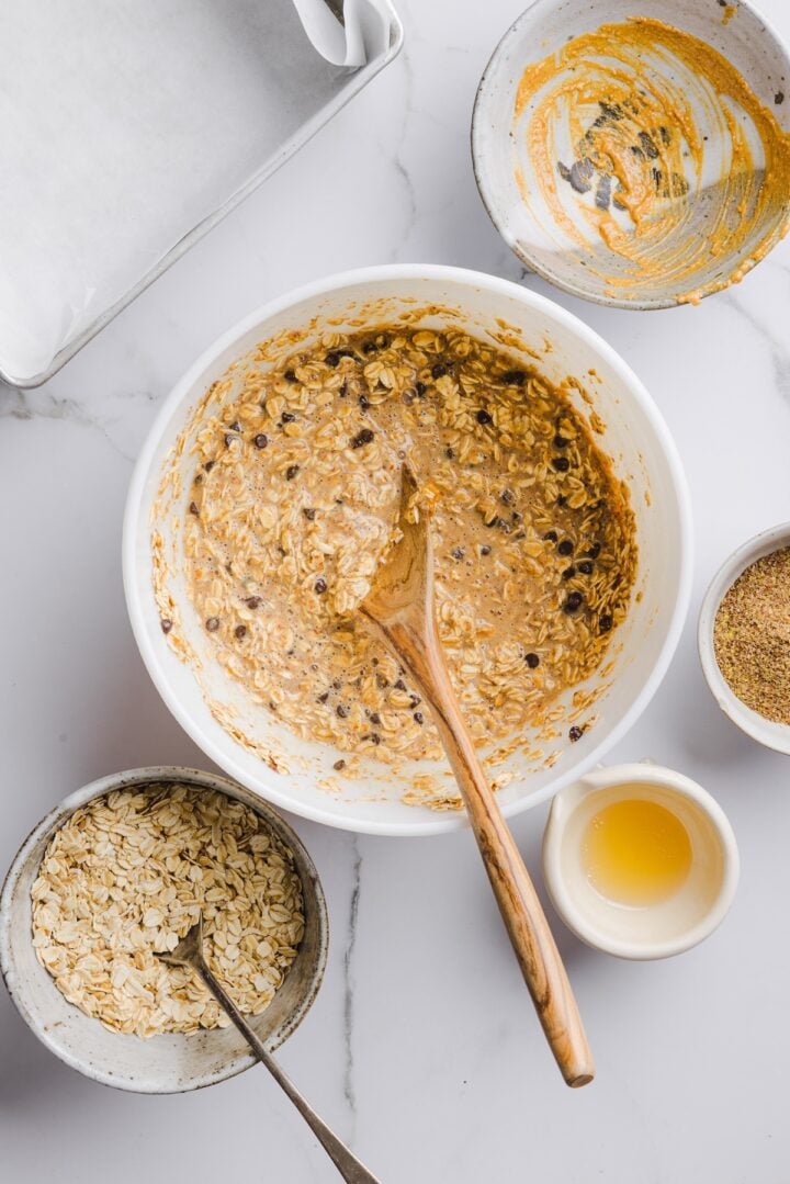 White mixing bowl with raw ingredients for peanut butter baked oatmeal mixed with a wooden spoon.
