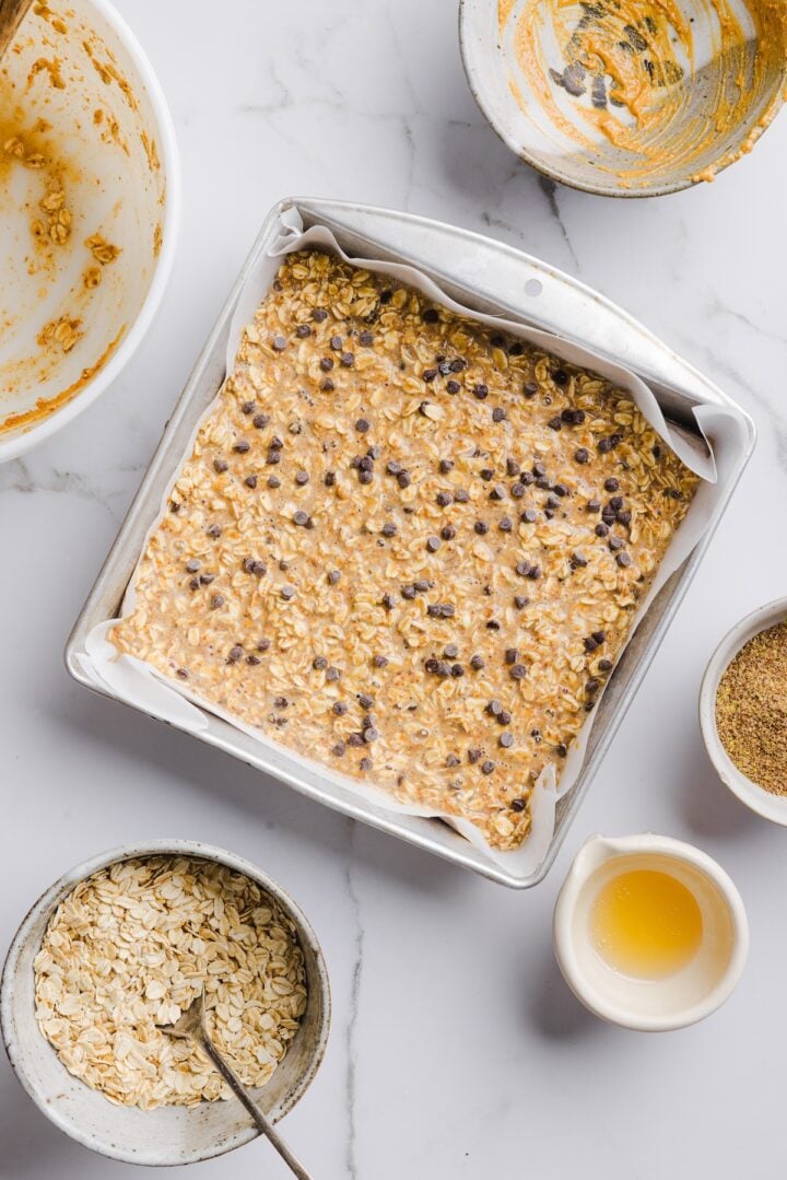 Peanut butter baked oats in a parchment-lined baking pan, topped with extra chocolate chips.