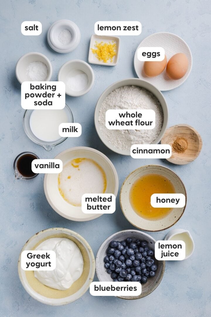 Labeled photo of ingredients for whole wheat blueberry muffins on a grey marble counter top.