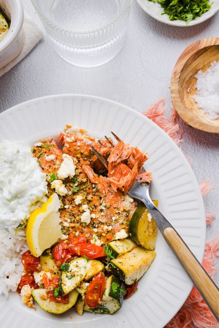 Salmon, rice, and roasted vegetables in a white bowl with tzatziki.