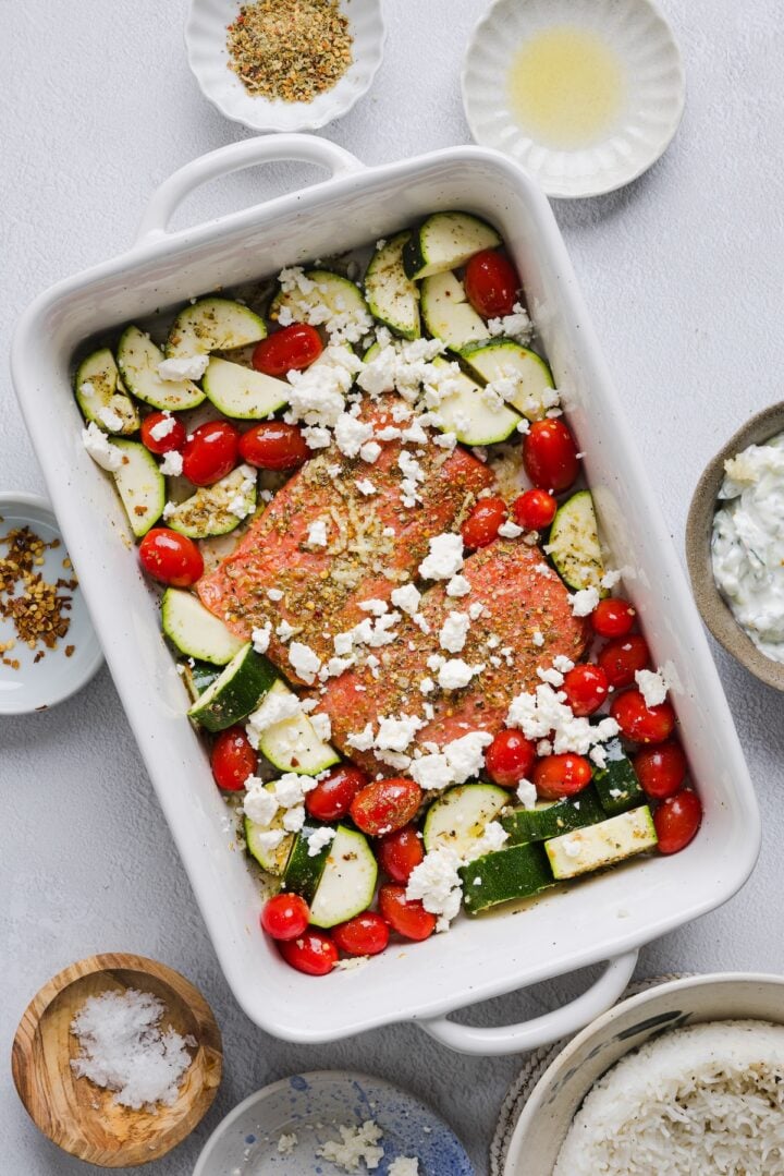 Salmon and vegetables in a large baking dish with feta sprinkled on top.