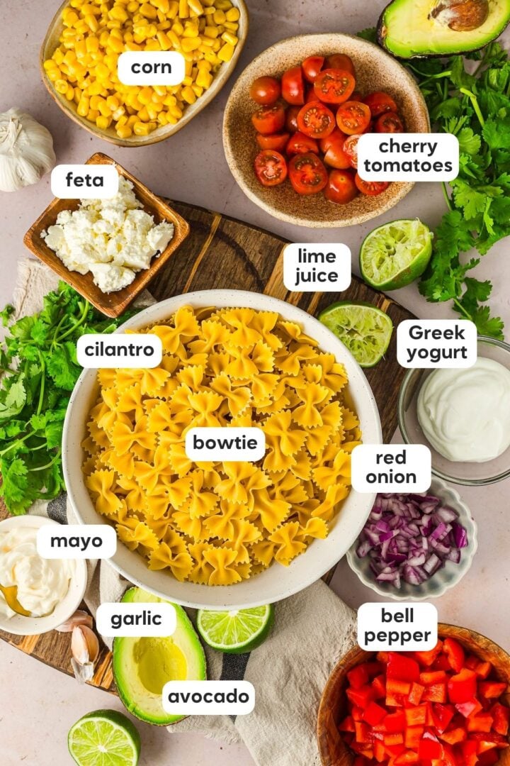 Labeled photo of ingredients for cilantro lime pasta salad, displayed in small bowls on a marble counter top.