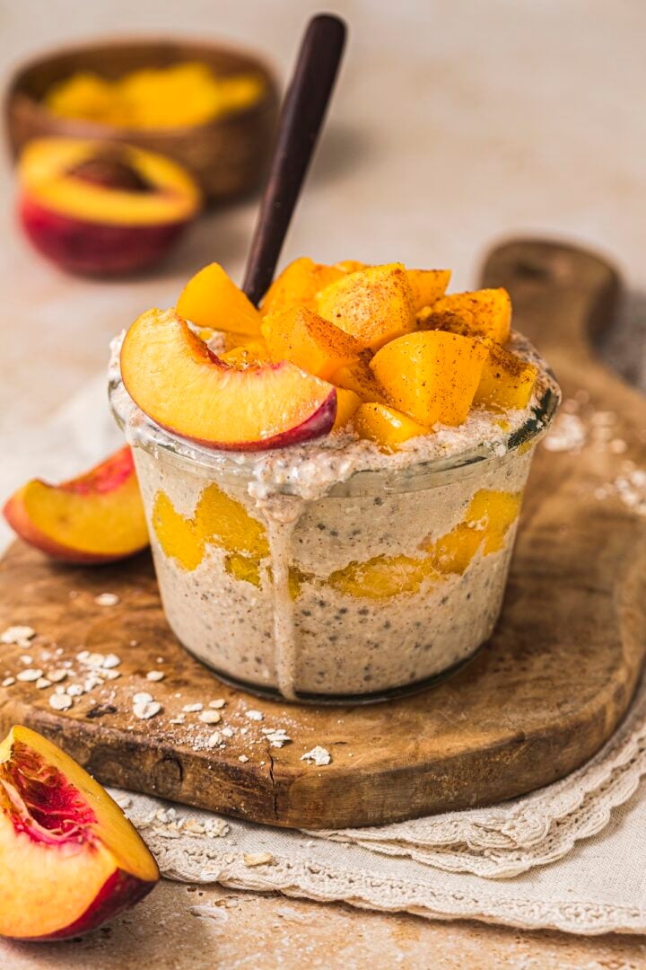 Peach Cobbler Overnight Oats in a glass jar, topped with extra peaches.