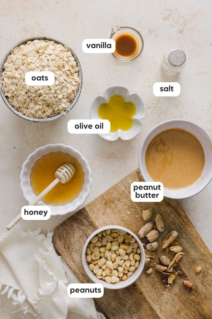 Ingredients for peanut butter granola displayed in small bowls on a grey marble counter.