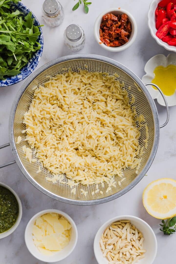 Orzo pasta cooked and drained, in a large silver bowl.