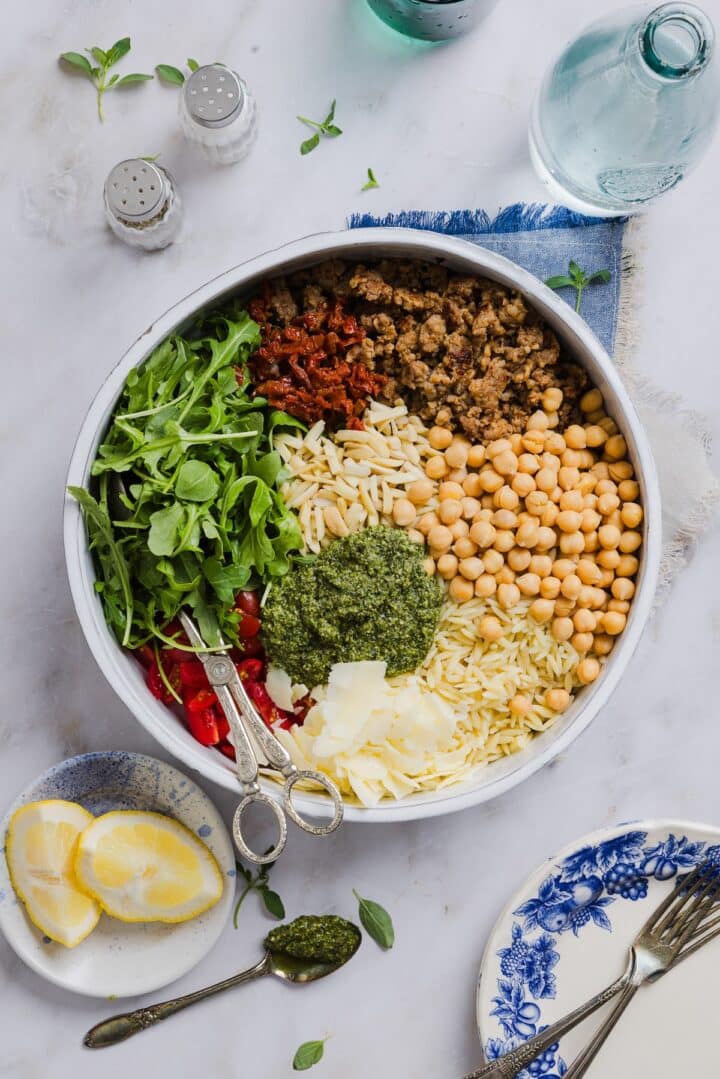 Ingredients for pesto and orzo salad in a large mixing bowl, unmixed.