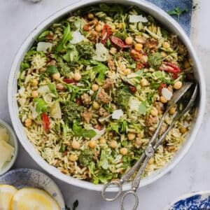 Pesto and orzo salad mixed in a large mixing bowl, with silver tongs.