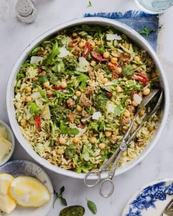 Pesto and orzo salad mixed in a large mixing bowl, with silver tongs.