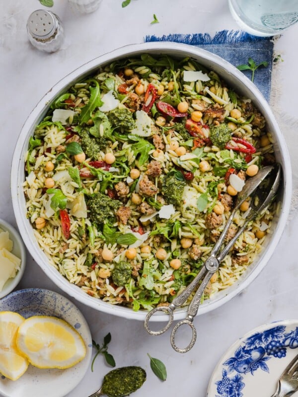 Pesto and orzo salad mixed in a large mixing bowl, with silver tongs.