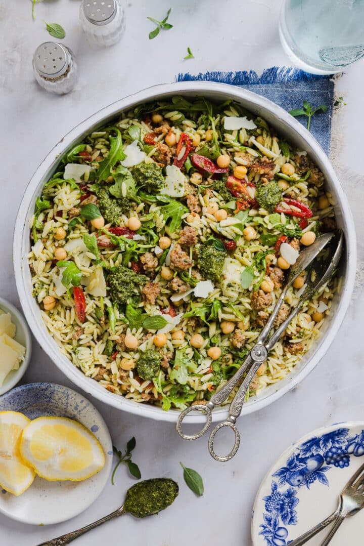 Pesto and orzo salad mixed in a large mixing bowl, with silver tongs.