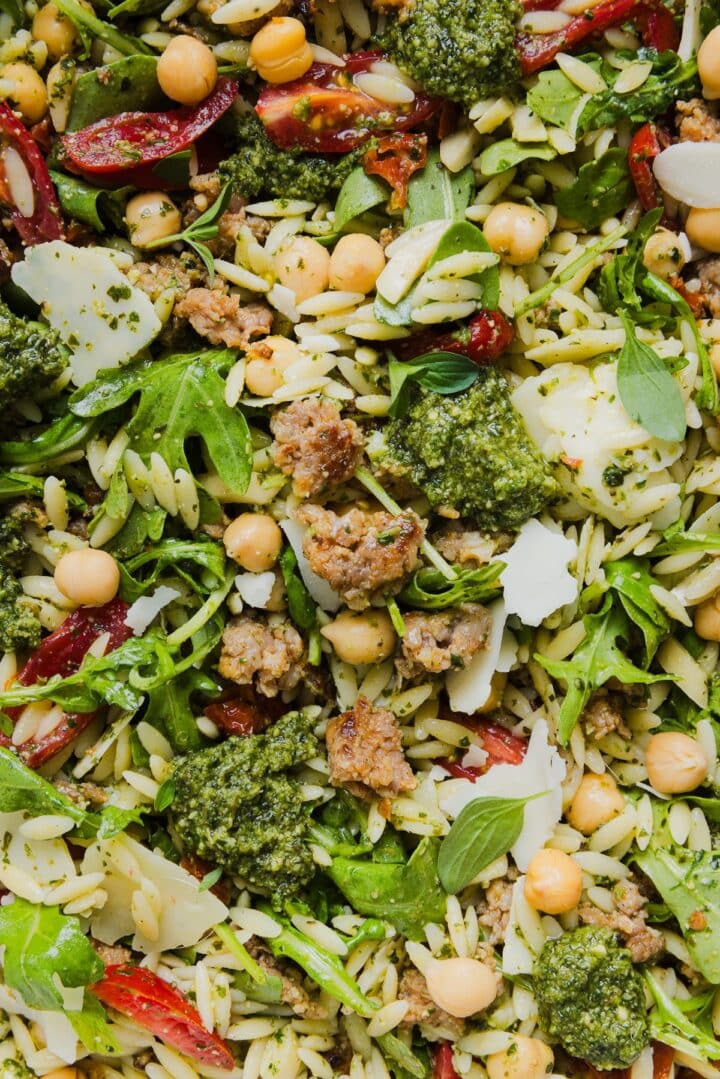 Close-up photo of pesto and orzo salad with Italian sausage in a large mixing bowl.