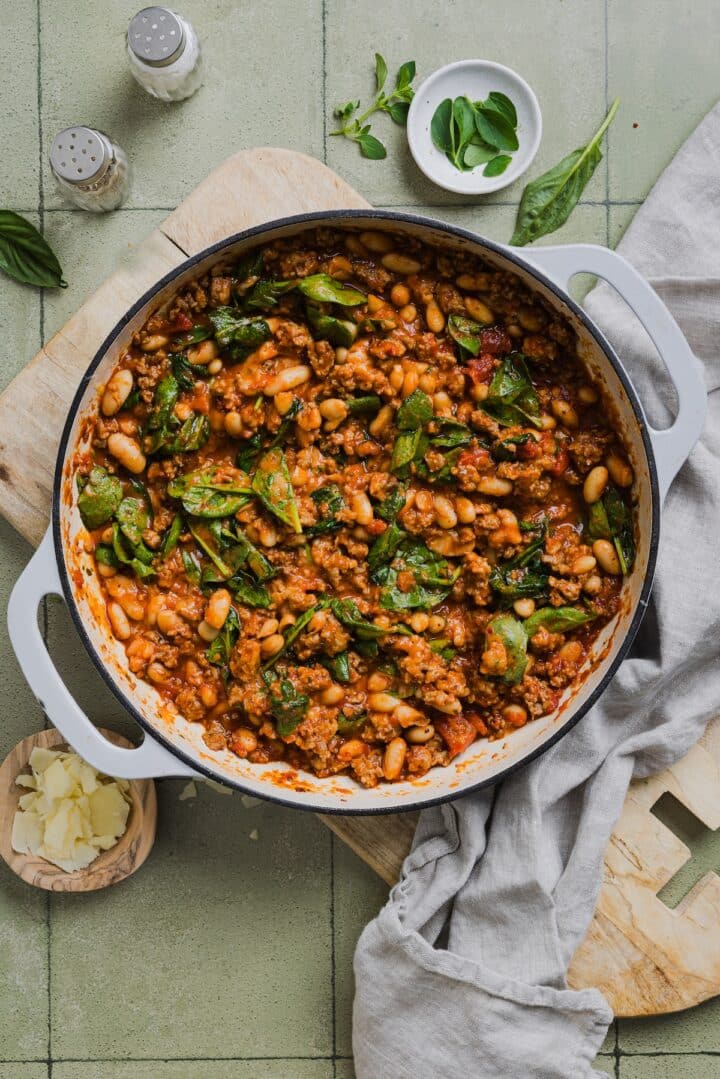 Baby spinach stirred into pizza beans in a large braiser pan.