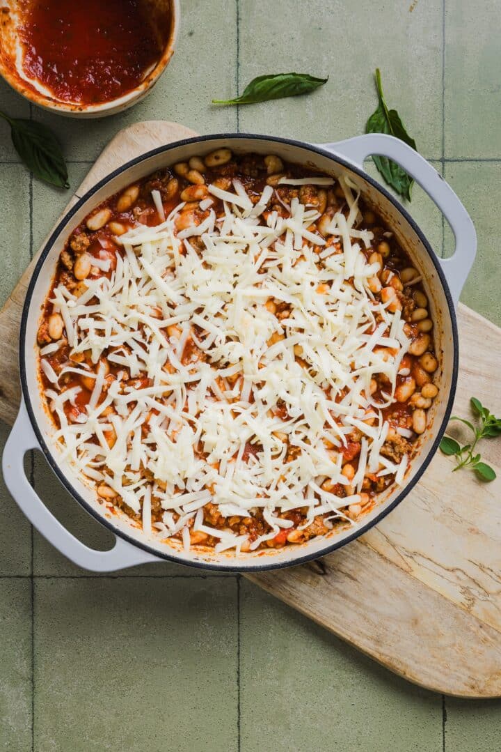Shredded mozzarella sprinkled over pizza beans in a braiser pan.