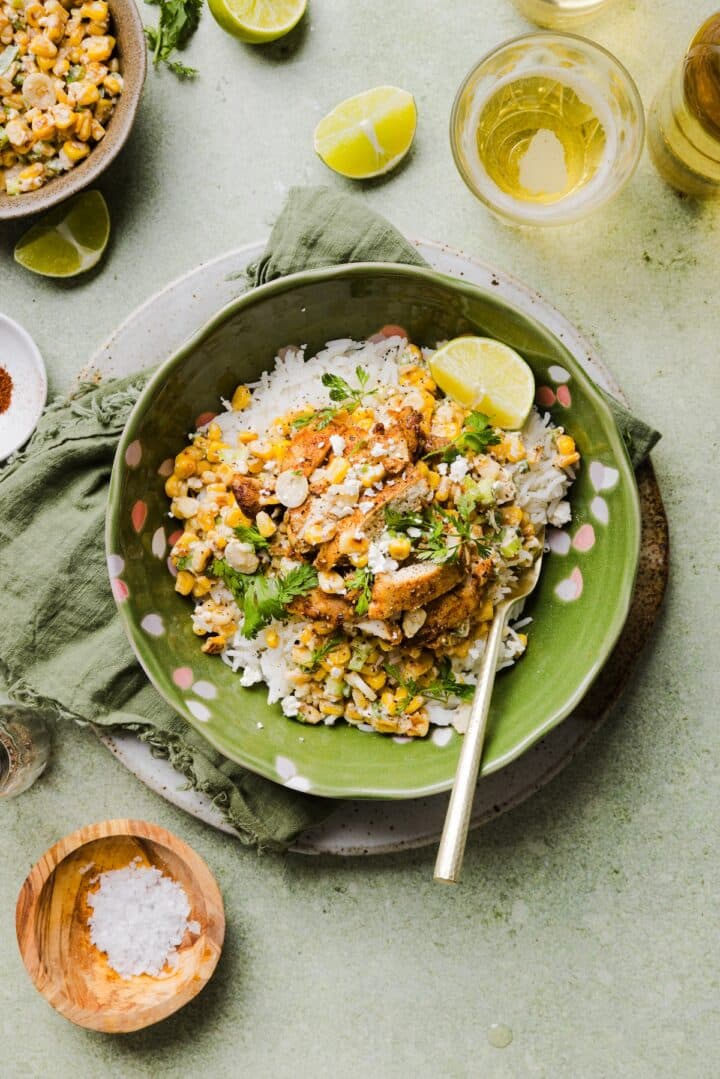 Street corn chicken and rice bowl in a green serving bowl with cilantro and a lime wedge.