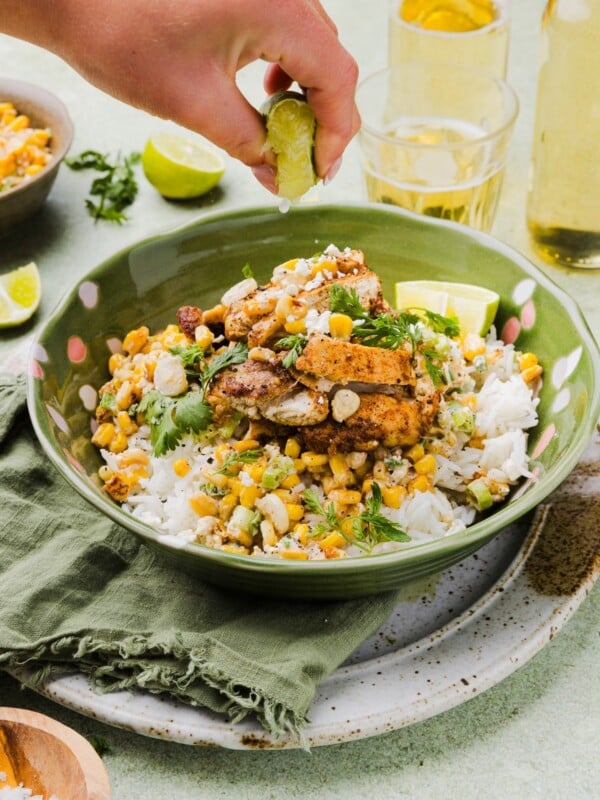 Mexican-inspired street corn chicken and rice bowl with a woman's hand squeezing a lemon wedge over top.