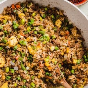 Ground beef fried rice in a large saute pan with a wooden spoon.