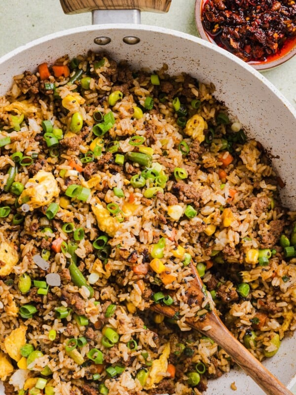 Ground beef fried rice in a large saute pan with a wooden spoon.