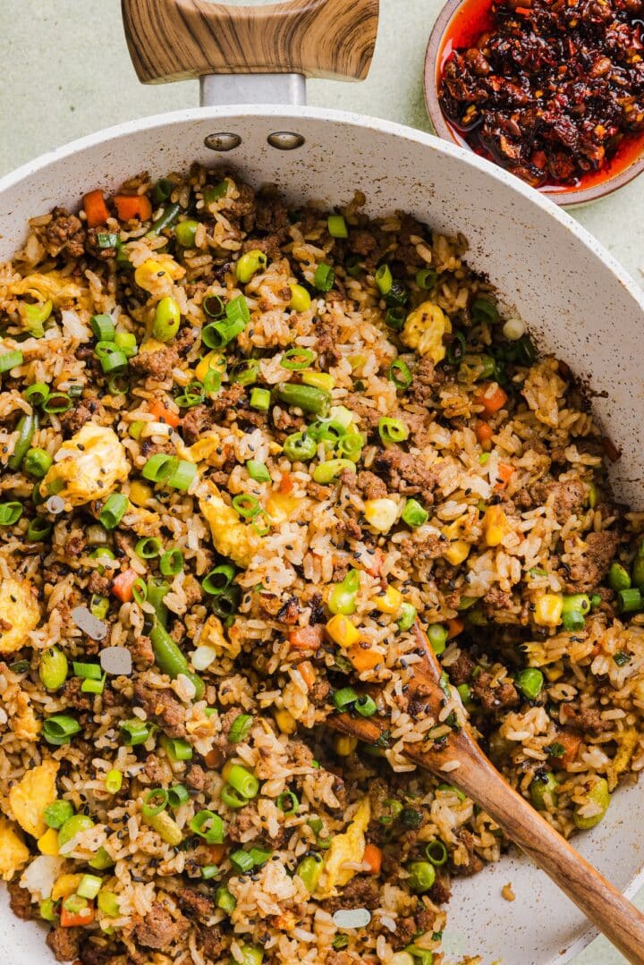 Ground beef fried rice in a large saute pan with a wooden spoon.