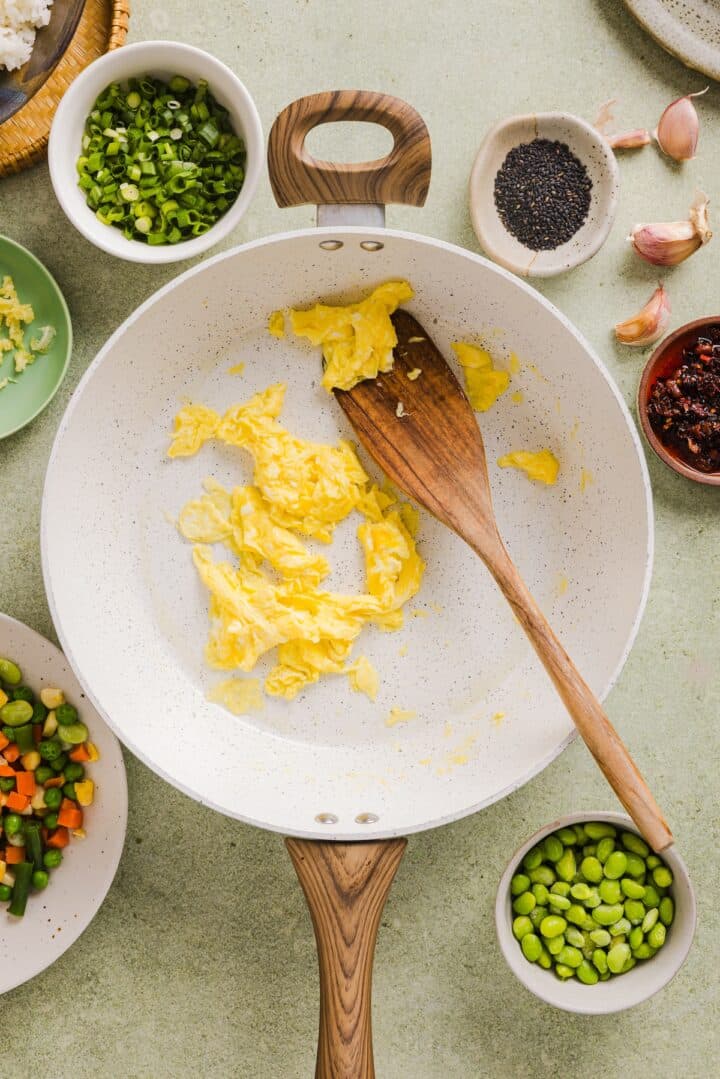 Eggs scrambled in a white pan with a wooden spoon.