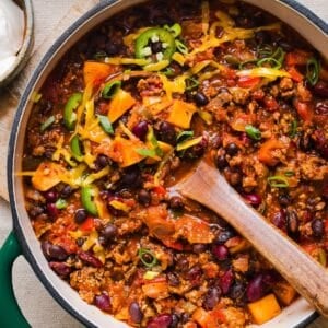 Healthy sweet potato turkey chili in a large pot, topped with shredded cheddar and green onions.
