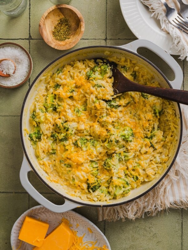 One-pot broccoli cheddar orzo in a braiser pan on a green tile counter.