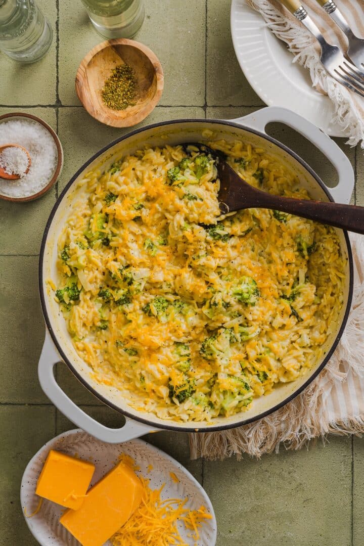 One-pot broccoli cheddar orzo in a braiser pan on a green tile counter.