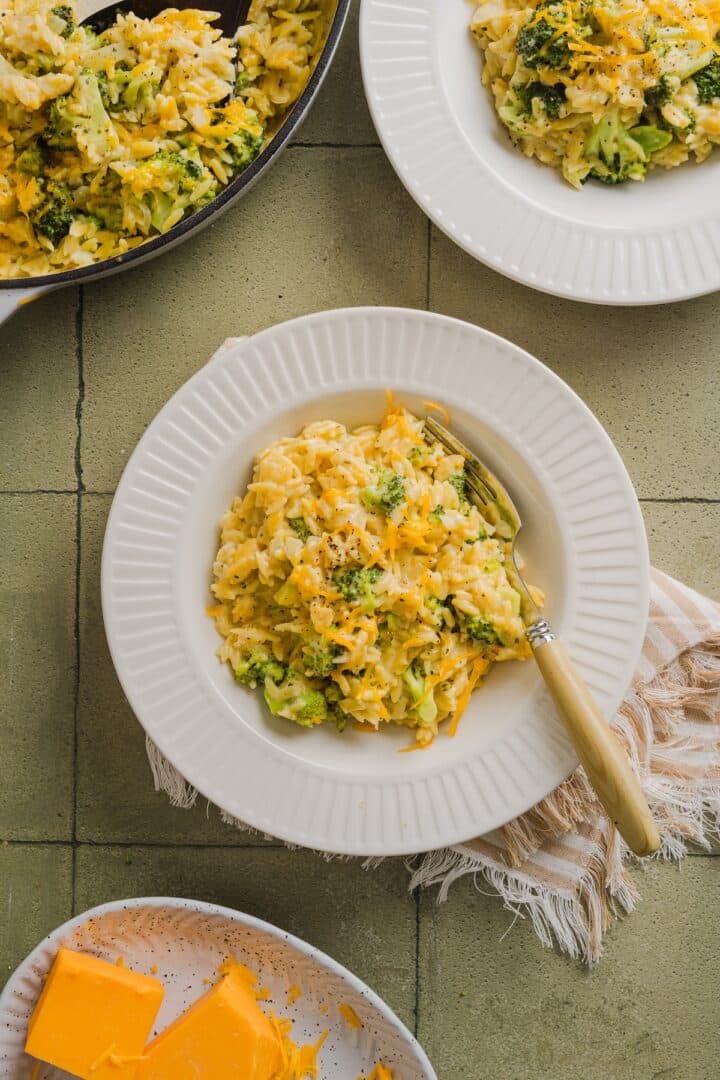 Broccoli cheddar orzo in a small white bowl on a green tile counter top.