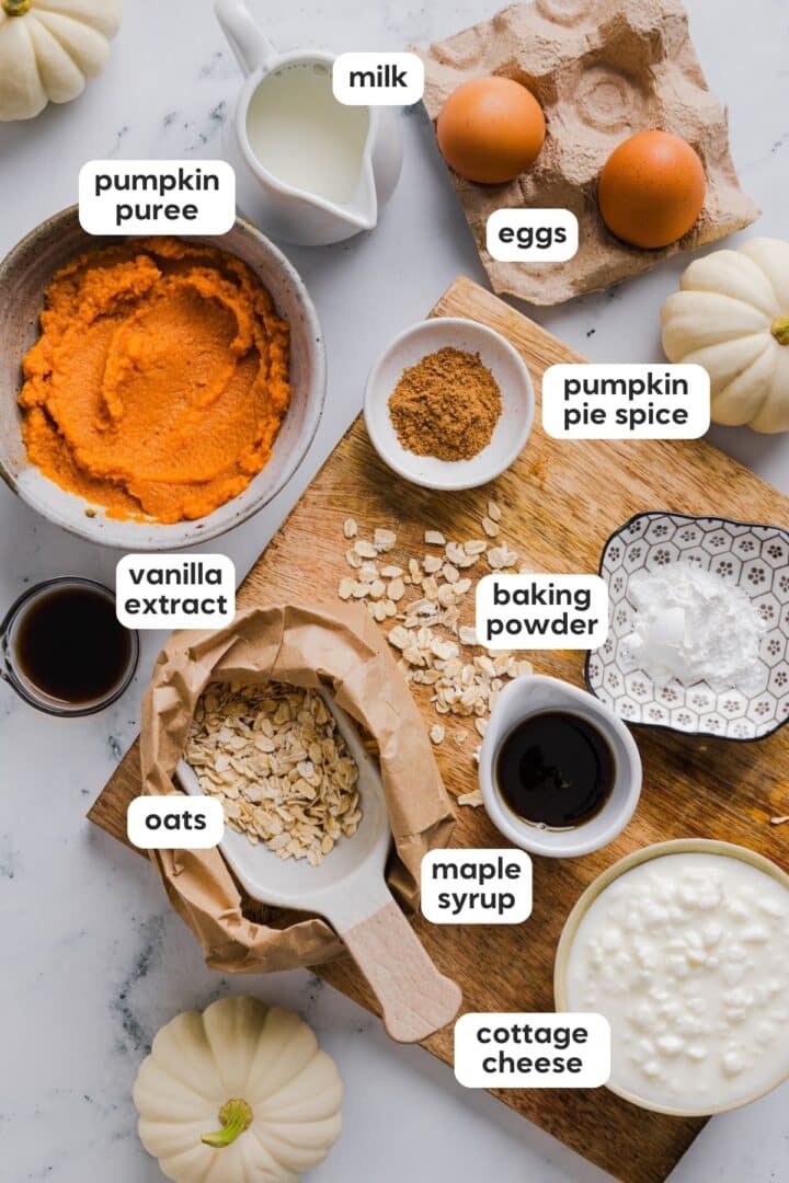 Ingredients for protein pumpkin pancakes with cottage cheese in small bowls on a marble counter.