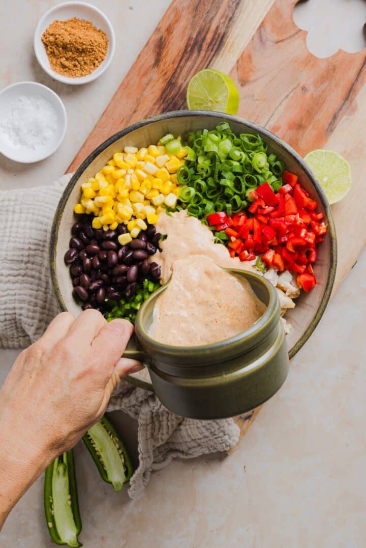 Southwest dressing being poured over top of southwest chicken salad ingredients in a large bowl.