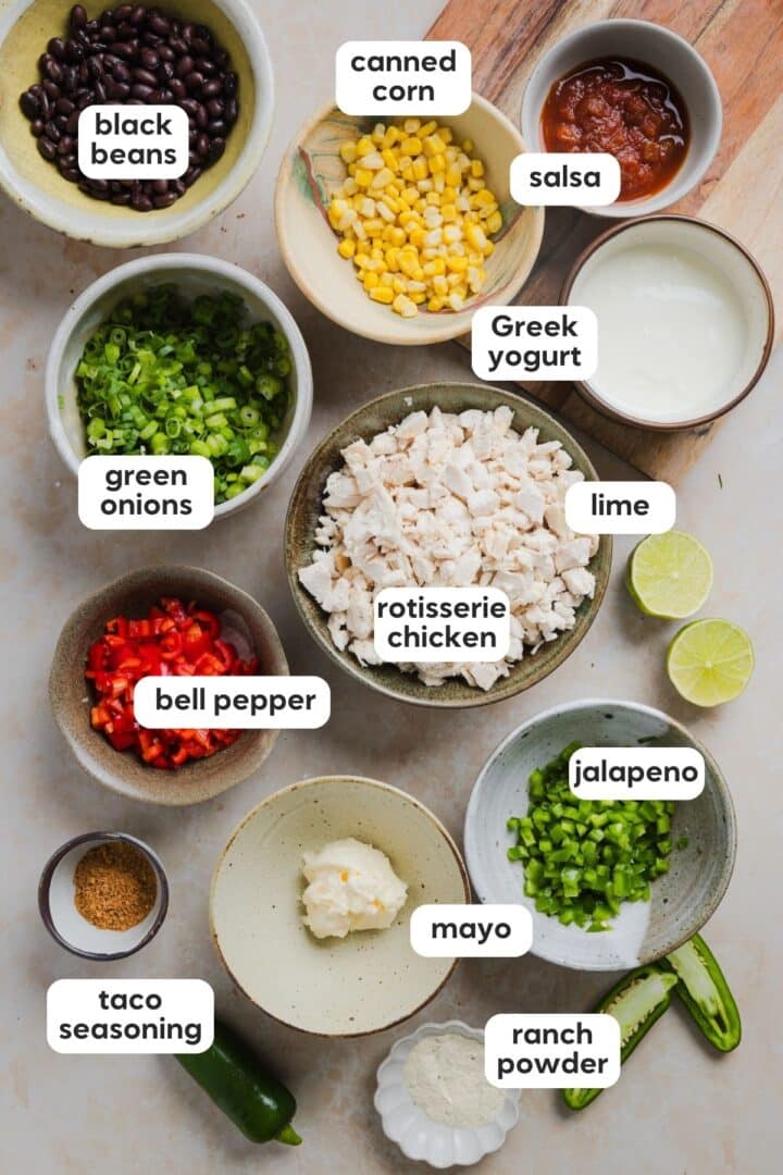 Labeled photo of ingredients for southwest chicken salad displayed in small bowls on a marble counter.