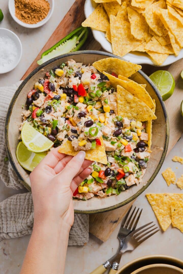 Southwest chicken salad being scooped with a tortilla chip with a woman's hand.